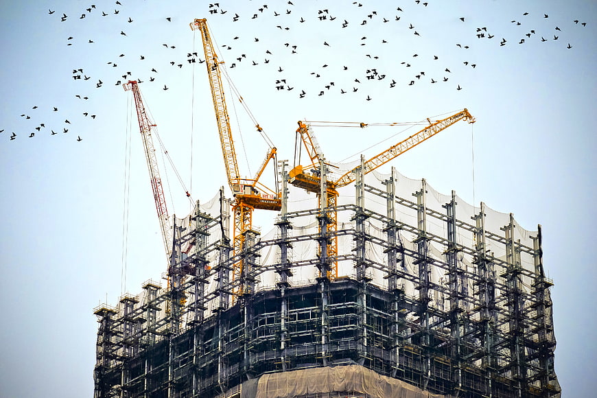 Construction cranes and flock of birds against blue sky