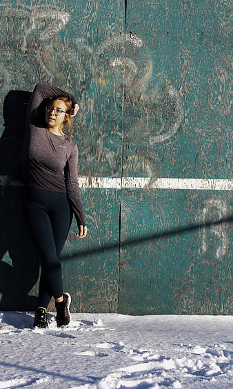 Woman in activewear posing against teal wooden wall in snow