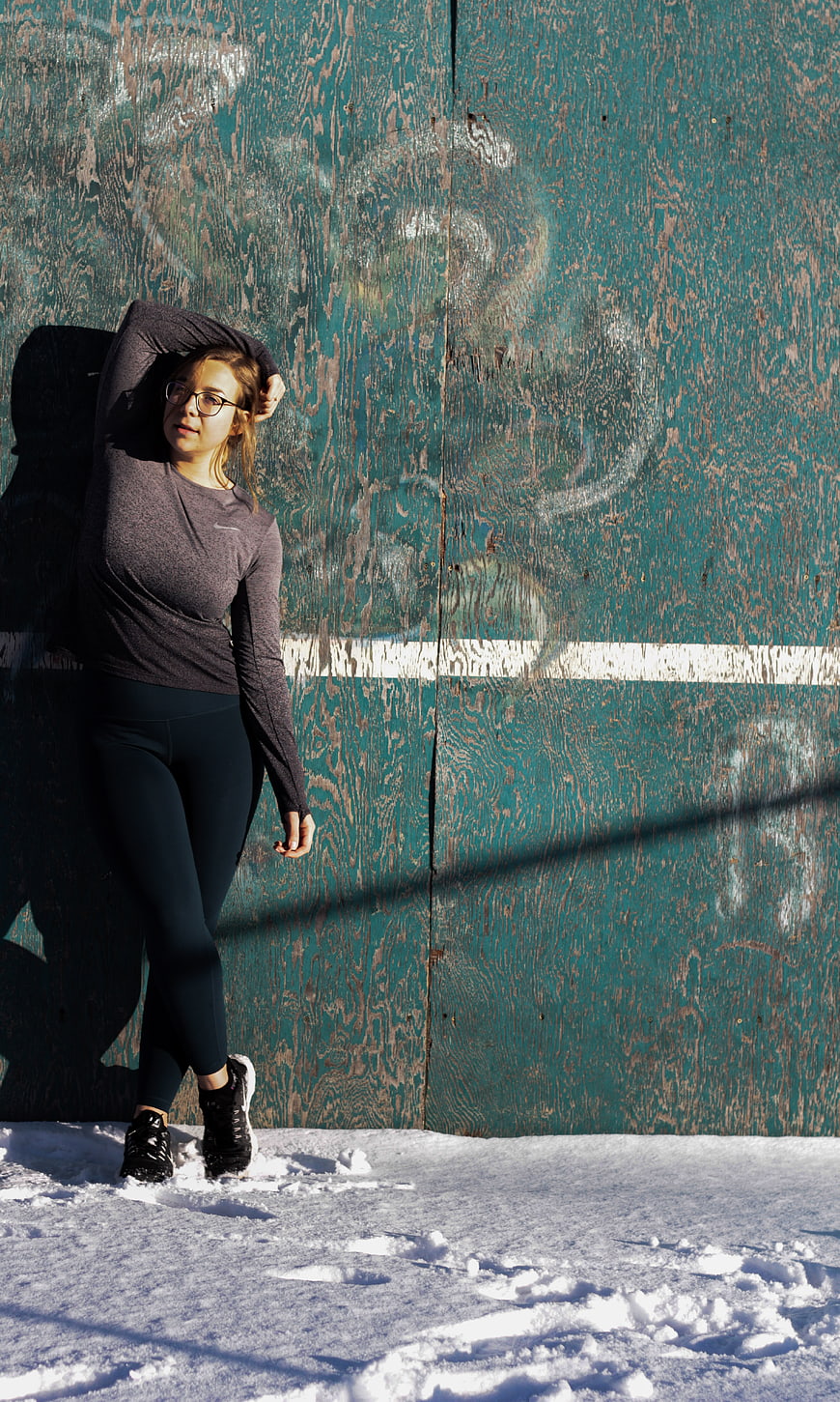 Woman in activewear posing against teal wooden wall in snow
