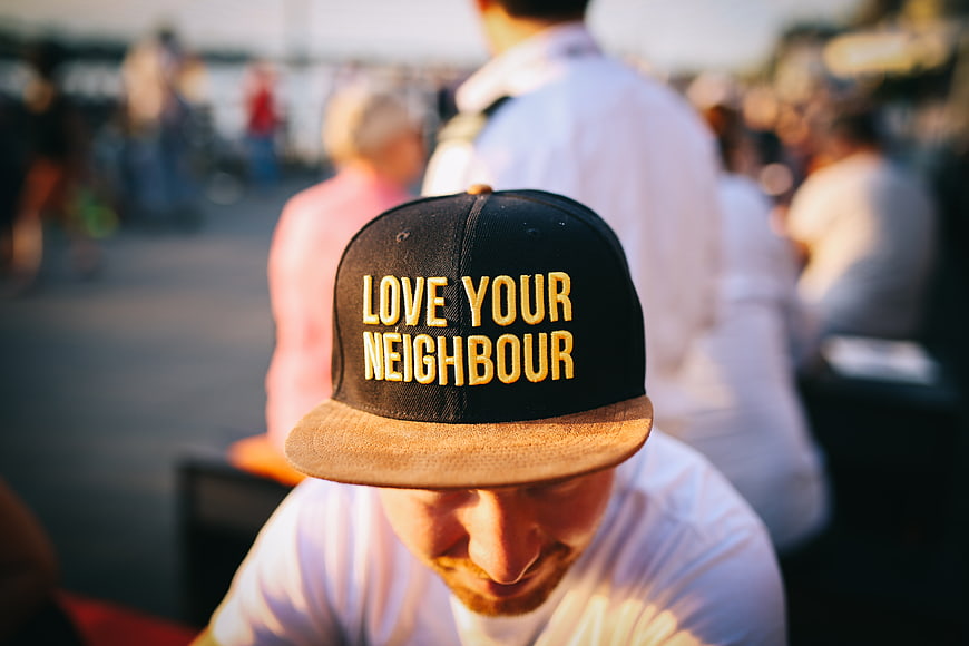 Man Wearing 'Love Your Neighbour' Cap in Crowd