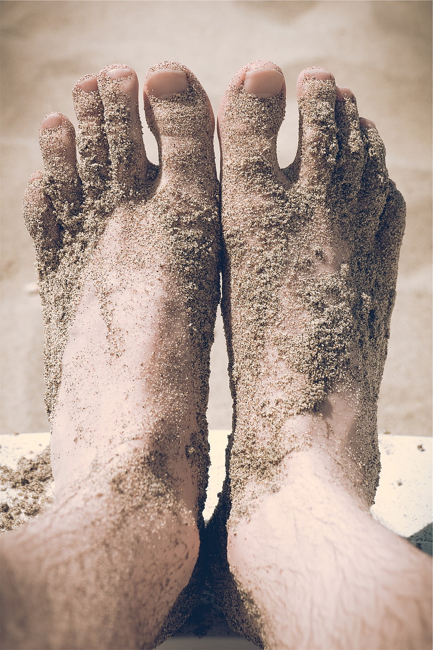 Close-up of bare feet covered in sand on a beach