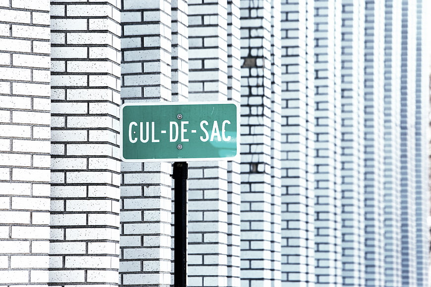 Green Cul-de-sac street sign against white brick wall