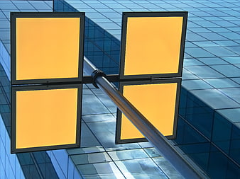 Four blank yellow square signs on a pole against a blue glass building