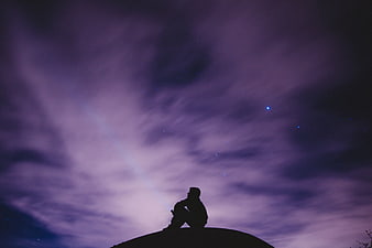 Silhouette of Man Sitting on Hill Under Purple Starry Sky