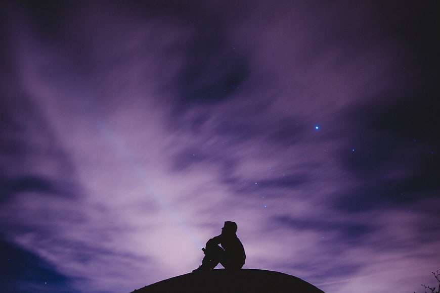 Silhouette of Man Sitting on Hill Under Purple Starry Sky
