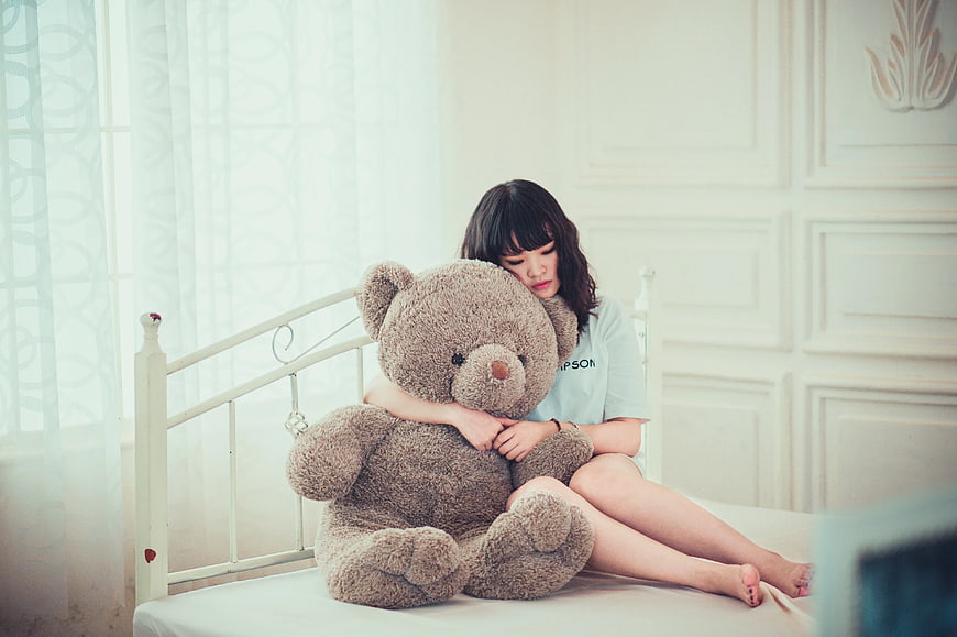 Sad Woman Hugging Large Teddy Bear on Bed