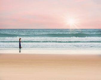 Woman standing on sandy beach at sunset with pink sky
