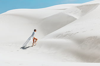 Woman in white dress running on white sand dunes