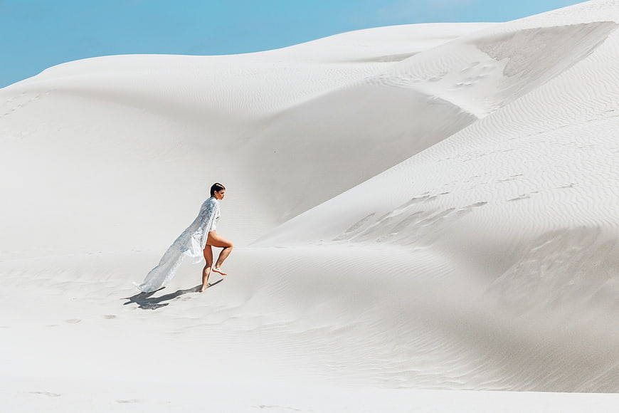 Woman in white dress running on white sand dunes