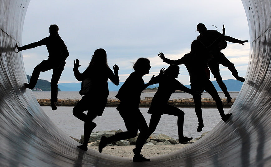 Silhouettes of friends jumping inside a large metal pipe