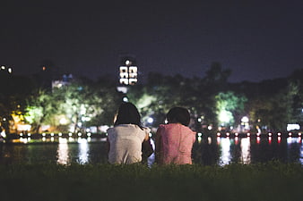 Couple sitting by lake at night with city lights
