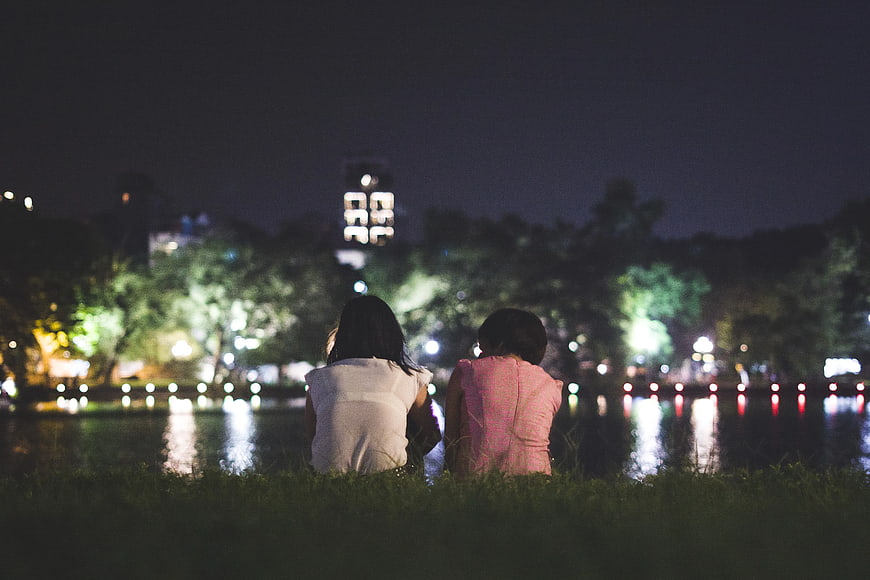 Couple sitting by lake at night with city lights