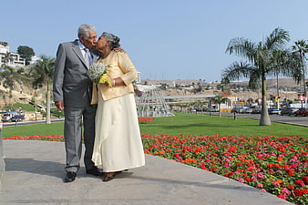 Senior couple sharing a kiss in a sunny park with flowers