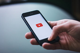 Hand holding smartphone with YouTube app icon on screen