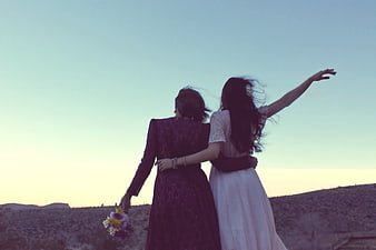 Two women in vintage dresses embracing in a desert landscape at sunset