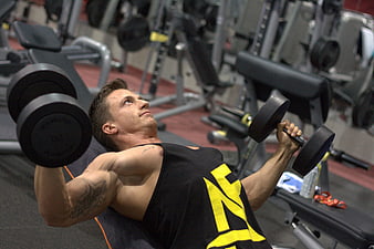 Muscular man performing dumbbell bench press in a commercial gym