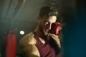 Intense male boxer training in gym with red gloves