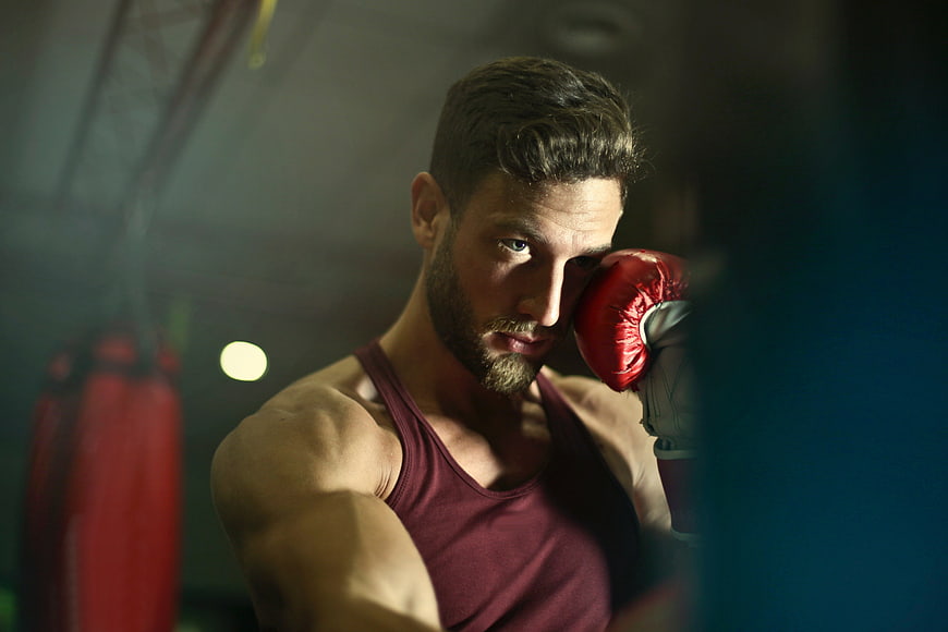 Intense male boxer training in gym with red gloves
