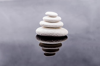 Stacked white zen stones with reflection on dark surface
