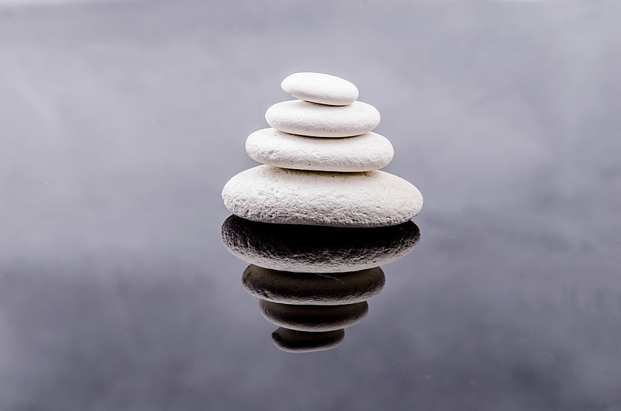 Stacked white zen stones with reflection on dark surface