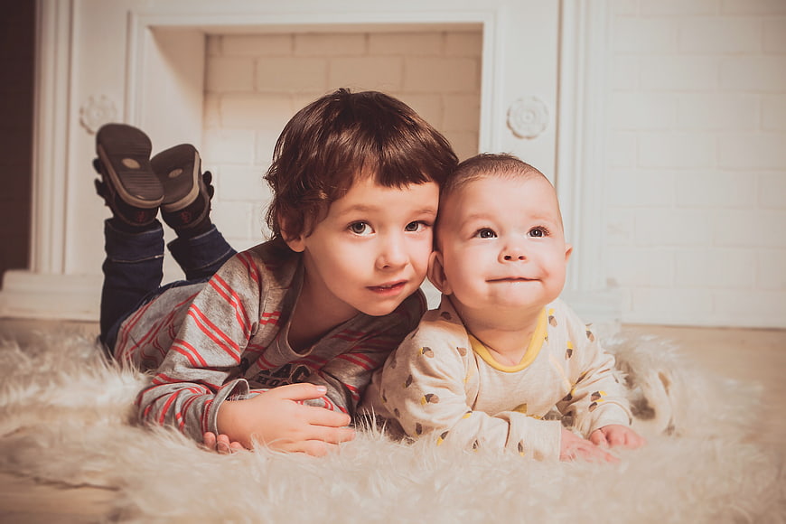 Cute Young Brother And Baby Boy Lying On Fluffy Rug