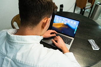 Man typing on laptop at dark wooden table