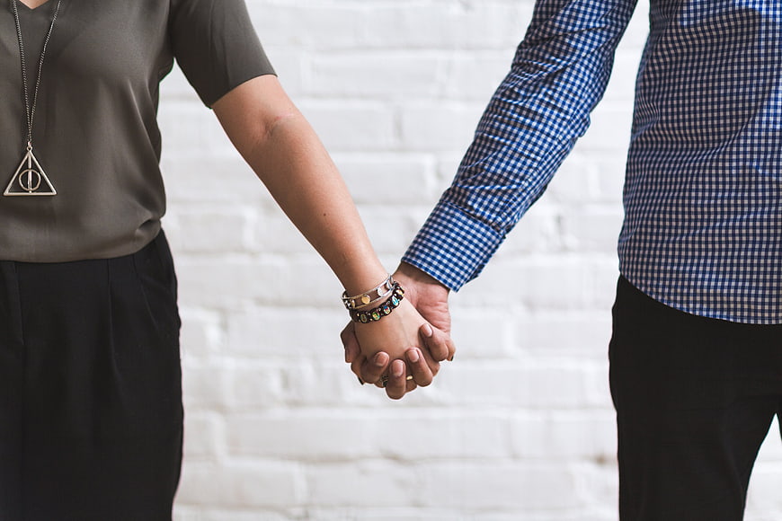 Couple Holding Hands Against White Brick Wall