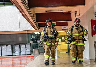 Two firefighters in full gear walking through a modern building interior