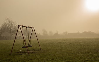 Empty swings in foggy park at sunrise