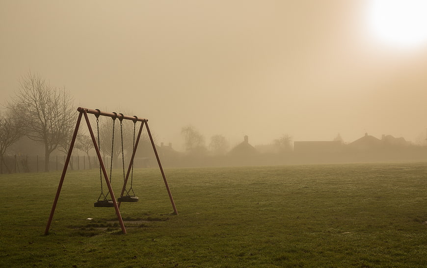 Empty swings in foggy park at sunrise