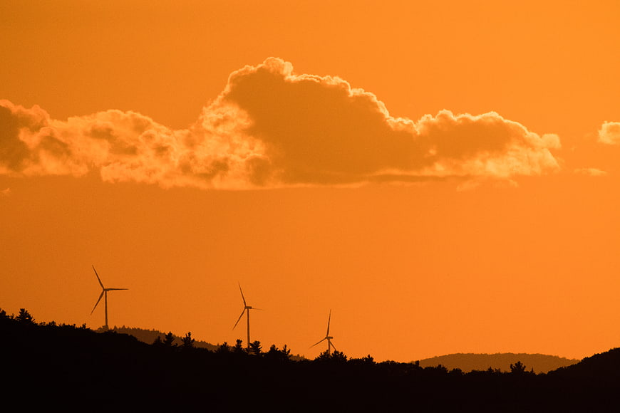 Silhouetted Wind Turbines Against Vibrant Orange Sunset Sky