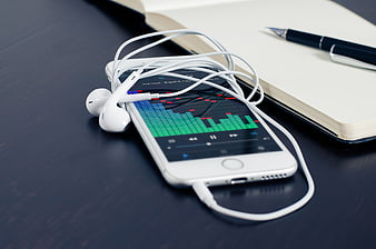 Smartphone with headphones and notebook on dark desk