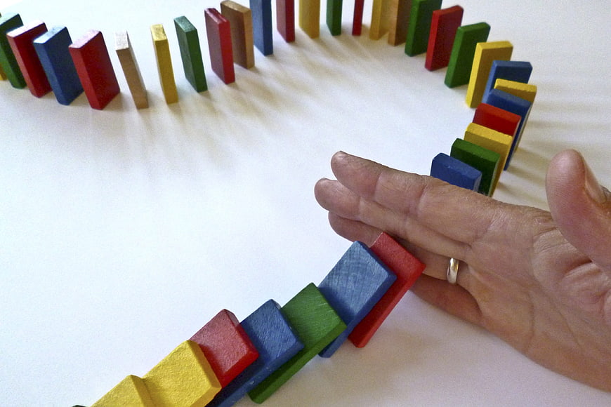 Hand Stopping Colorful Domino Chain Reaction On White Surface