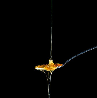Golden Honey Dripping from Silver Spoon on Black Background