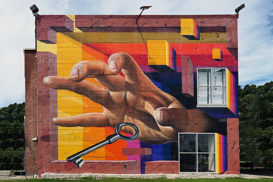 Colorful Mural of Hand Reaching for Key on Brick Wall