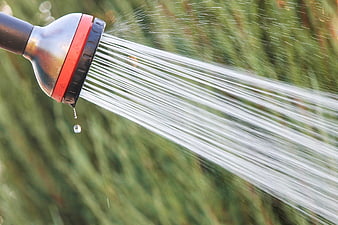 Garden Hose Nozzle Spraying Water Against Blurred Green Grass Background