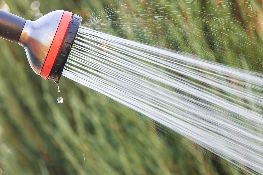 Garden Hose Nozzle Spraying Water Against Blurred Green Grass Background