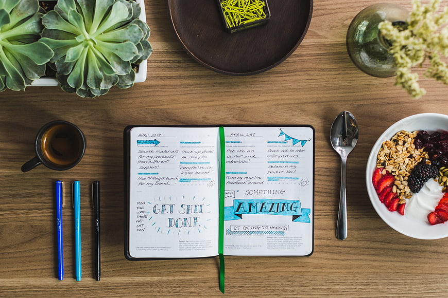 Flat lay of open planner, healthy breakfast, and office supplies
