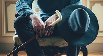 Man with tattoos holding cane and hat on vintage chair