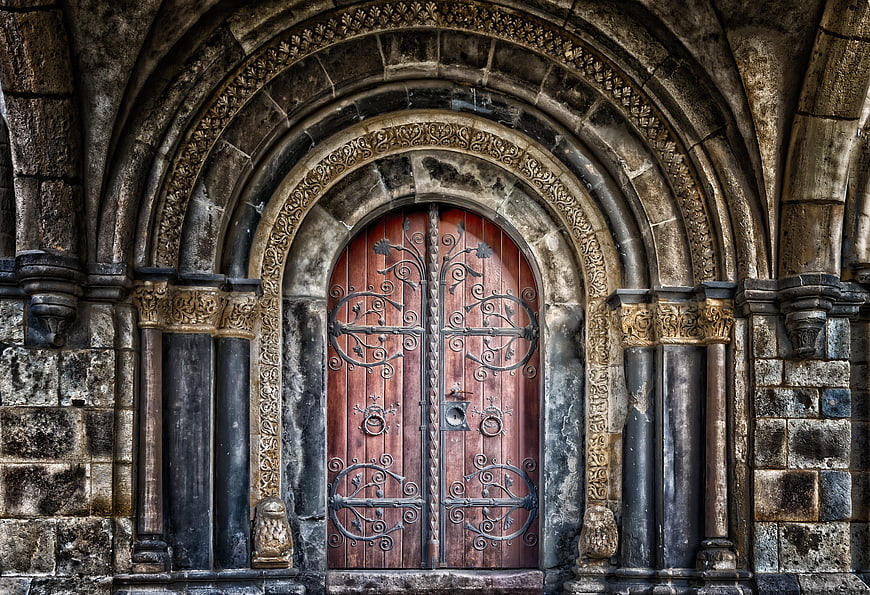 Ancient arched wooden door with ornate ironwork and stone facade