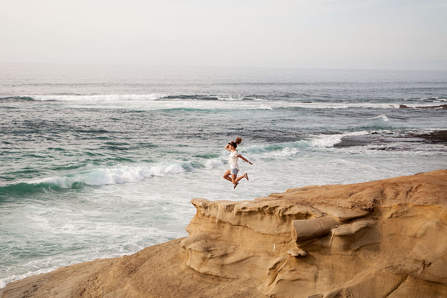 Woman jumping off coastal cliff into ocean waves