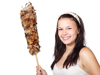 Smiling young woman holding feather duster on white background