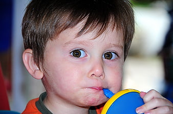 Close-up of a young boy drinking from a blue and yellow cup