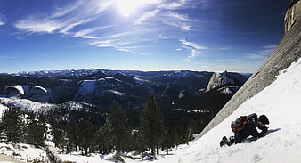 Man climbing snowy granite slope with mountain valley view