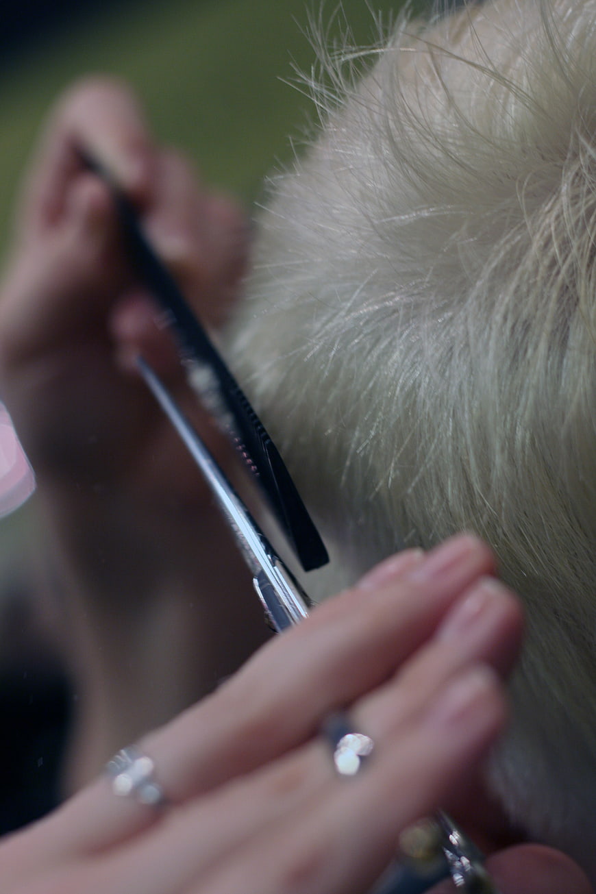 Close up of hairdresser cutting blonde hair with scissors