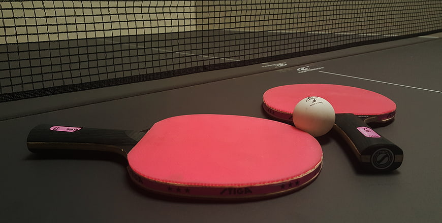 Two red table tennis paddles and a white ball on a dark indoor table