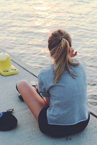 Woman sitting by water at sunset looking at view