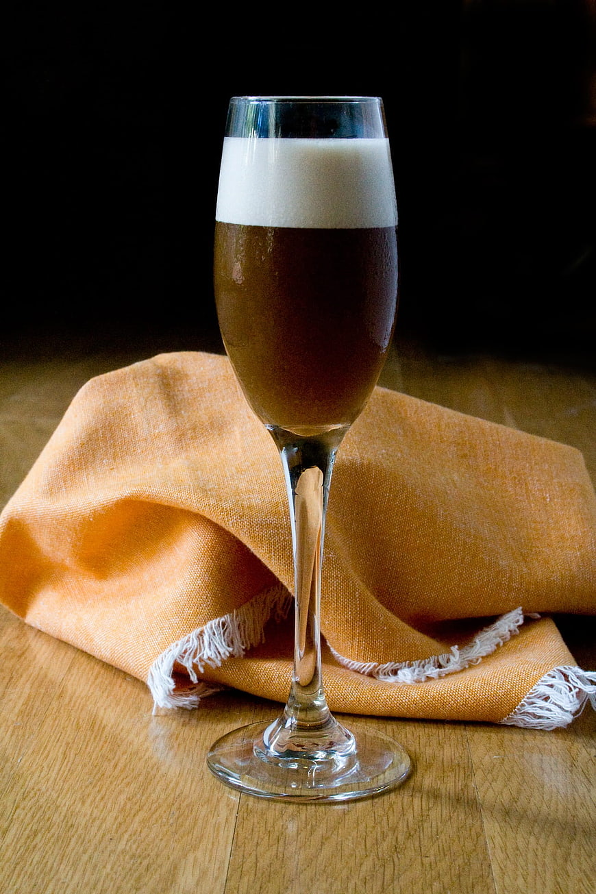 Glass of dark beer with foam on wooden table