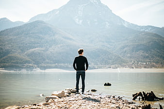 Man standing on rocky shore contemplating misty mountain lake landscape