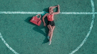 Aerial view of woman lying on green soccer field with red bag